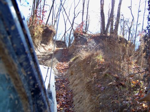 1987 Ford F-250 - Driving through a wooded area on a challenging off-road trail, with fallen leaves covering the ground.