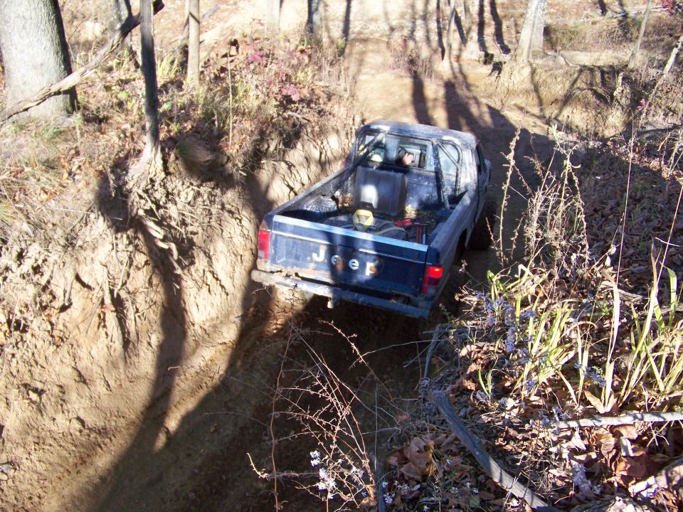 Jeep pickup truck with roll bar driving on a narrow dirt trail in woods