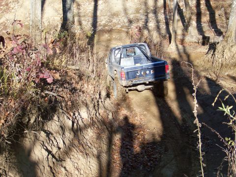 1987 Ford F-250 - A Jeep pickup truck navigates a muddy, wooded trail.