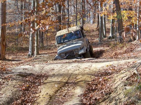 1987 Ford F-250 - A Jeep Wrangler is stuck in a ditch on a wooded trail during autumn.