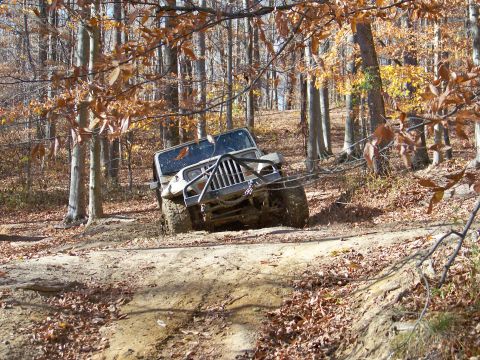 1987 Ford F-250 - Jeep Wrangler navigating a muddy trail through autumn woods.