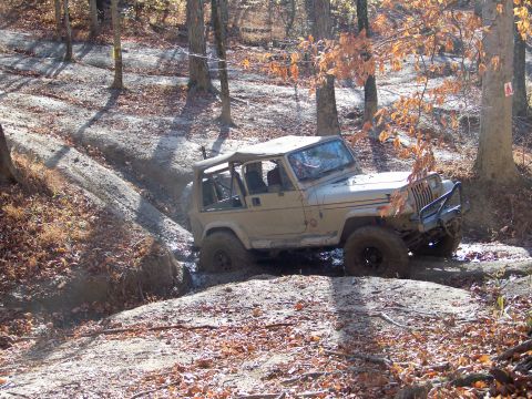 1987 Ford F-250 - A Jeep Wrangler tackles a challenging off-road course with muddy terrain and fallen leaves.