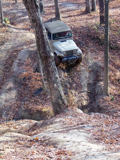 1987 Ford F-250 - A tan Jeep Wrangler navigates a challenging off-road course in a wooded area during autumn.