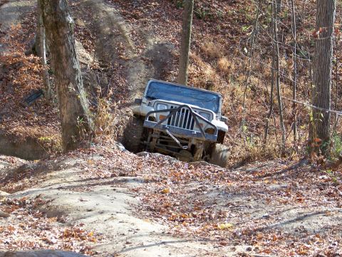 1987 Ford F-250 - A white Jeep Wrangler TJ navigates a challenging off-road trail surrounded by trees and fallen leaves.