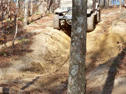 1987 Ford F-250 - An off-road vehicle navigates a steep, muddy incline in a wooded area.
