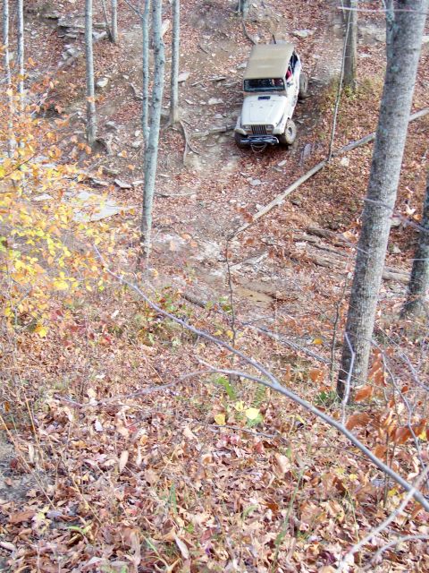1987 Ford F-250 - Jeep Wrangler navigates a challenging off-road trail through a forest during the fall season.