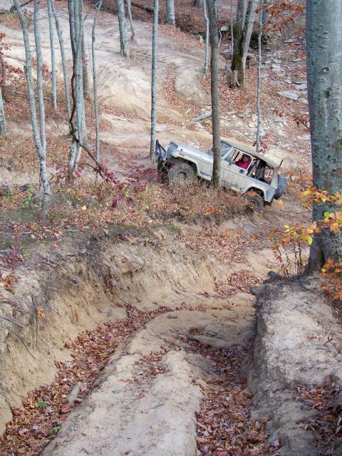 1987 Ford F-250 - An off-road vehicle navigates a steep, muddy trail through a wooded area during autumn.
