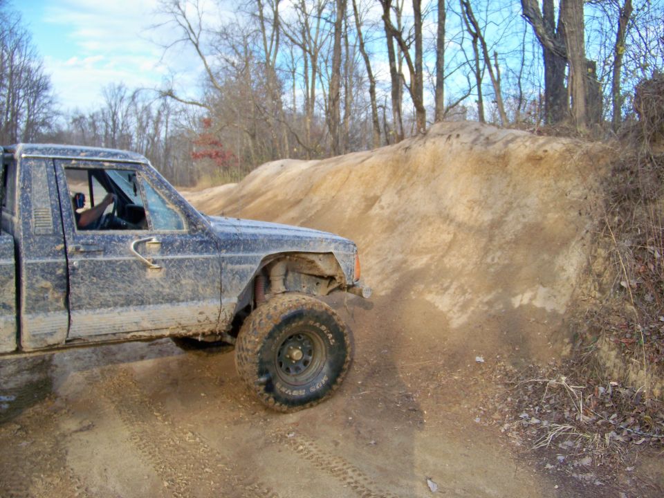 Muddy pickup truck driving on a dirt hill with trees in the background