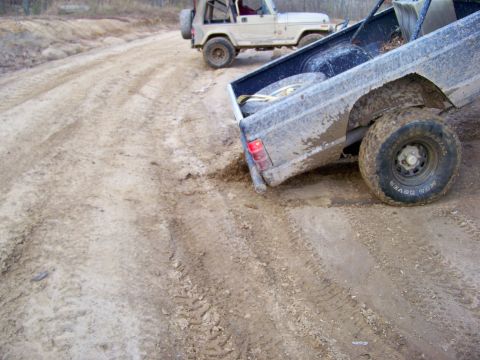 1987 Ford F-250 - Two off-road vehicles navigate a challenging muddy track, kicking up dirt.