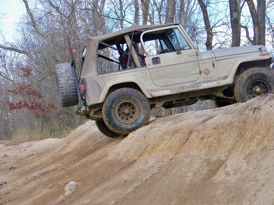 Tan Jeep Wrangler on a rocky incline, spare tire mounted on rear, soft top