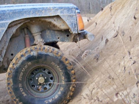 1987 Ford F-250 - Off-road vehicle navigating a sandy incline, showing mud-caked tire and suspension components.