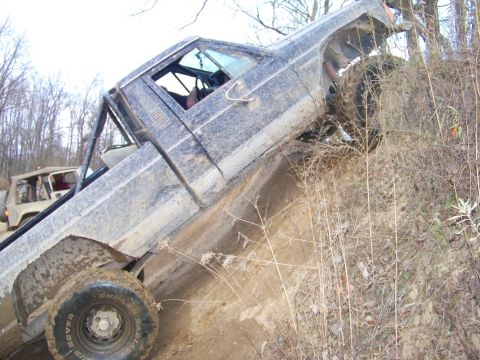 1987 Ford F-250 - A dark pickup truck is stuck on a steep, muddy hill with another vehicle in the background.