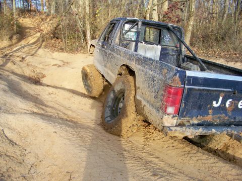 1987 Ford F-250 - Jeep Comanche stuck in mud on an off-road trail, showing its rear end and lifted suspension.