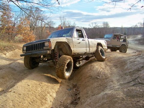1987 Ford F-250 - A lifted Jeep Comanche navigates a challenging dirt path, with another Jeep following behind.