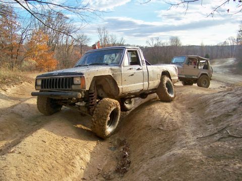 1987 Ford F-250 - A lifted Jeep Comanche navigates a challenging off-road course, followed closely by another Jeep.