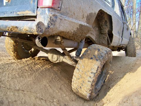 1987 Ford F-250 - Off-road truck's rear suspension and tire covered in mud on a dirt trail.