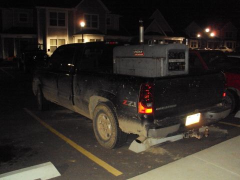 2003 Chevrolet Silverado 1500 - A black 2003 Chevrolet Silverado 1500 pickup truck is parked at night, loaded with a Lincoln welding machine in its bed.