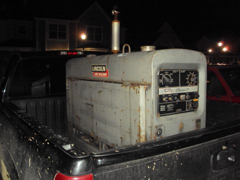 2003 Chevrolet Silverado 1500 - A Lincoln Arc Welder is loaded into the bed of a black pickup truck at night.