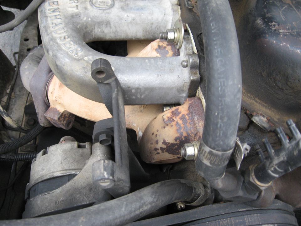Engine bay close-up with aluminum manifold, rusty cast parts, bolts and rubber hoses