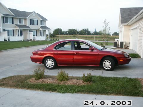 1998 Mercury Sable - A red 1998 Mercury Sable sedan is parked in a driveway next to a residential building.