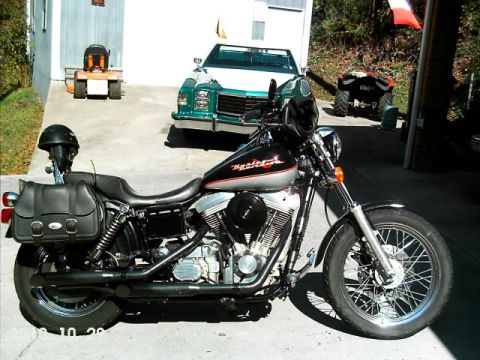 1996 Harley-Davidson Super Glide - A Harley-Davidson motorcycle is parked in a driveway with other vehicles and a riding mower in the background.