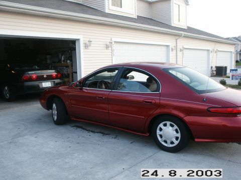 1998 Mercury Sable - A red 1998 Mercury Sable is parked in front of a garage, with another dark-colored car visible inside.