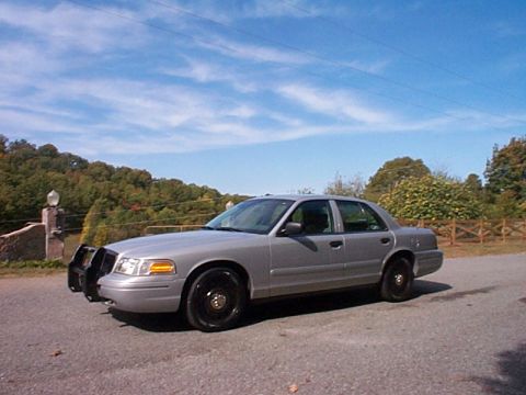 2004 Ford Crown Victoria - Silver 2004 Ford Crown Victoria sedan, likely a former police car, seen from the front-three-quarter view.