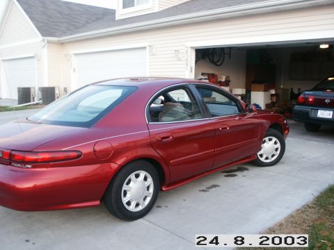 1998 Mercury Sable - Side view of a red 1998 Mercury Sable parked in front of a residential garage, with another vehicle inside.