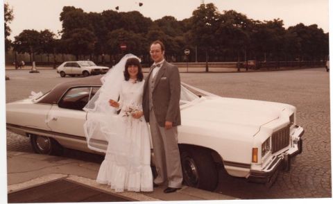 1991 Ford Crown Victoria - A newly married couple poses with their wedding car, a large sedan, with another vehicle in the background.