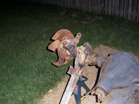 1992 Ford Bronco - A heavily rusted vehicle axle assembly is supported by jack stands on a grassy area.