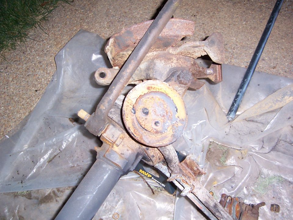 Rusty steering gear assembly with yellow circular component and metal rod, on plastic sheeting