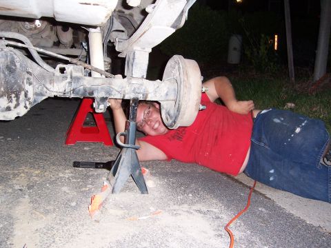 1992 Ford Bronco - A person works on the rear axle of a vehicle, which is raised on jack stands.