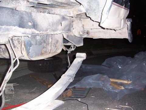1992 Ford Bronco - The rear suspension of a vehicle is shown with a leaf spring detached and a spare tire beneath the fuel tank.