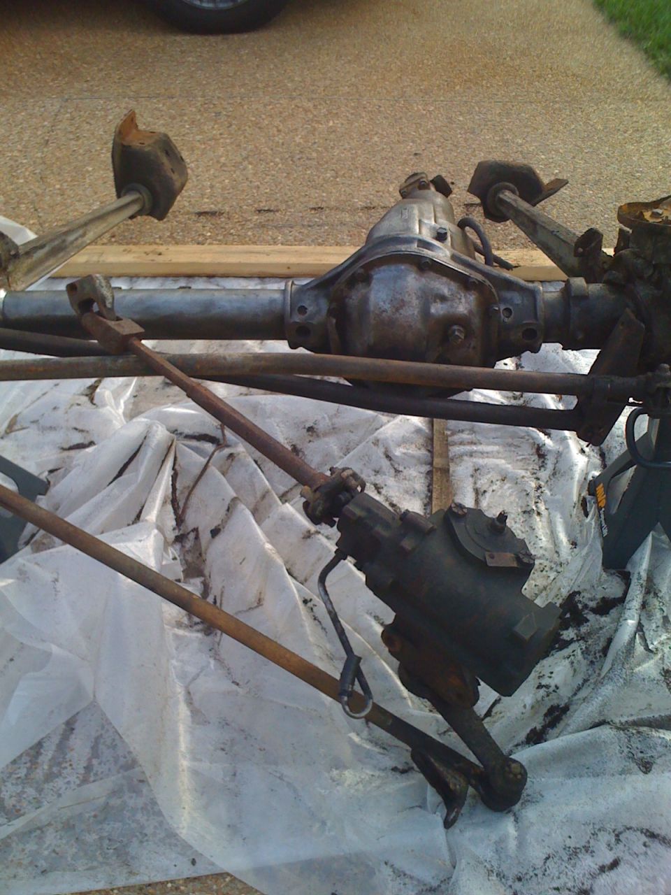 Front axle assembly with steering box and tie rods, likely from a Ford Bronco