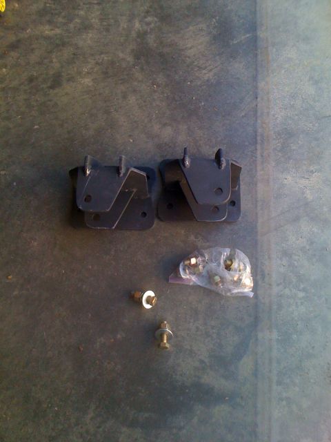 1992 Ford Bronco - Two black metal brackets and a bag of hardware are laid out on a dark, textured surface.
