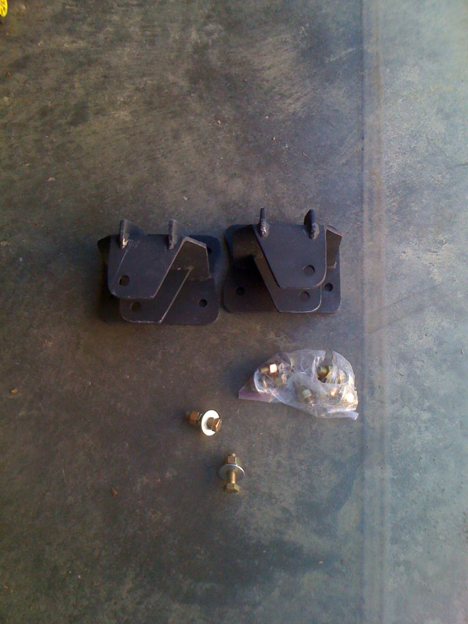 Two black metal brackets and a bag of hardware on a dark surface