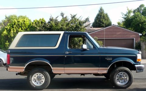 1995 Ford Bronco - Side profile of a dark blue 1995 Ford Bronco with tan lower body trim and a white removable top.