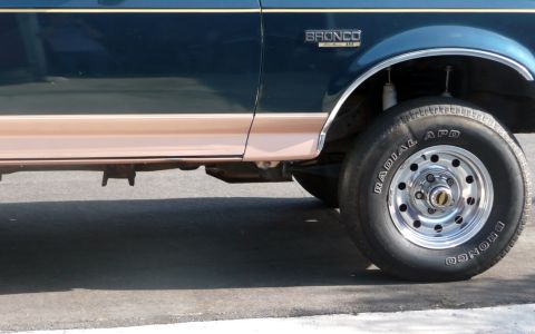 1995 Ford Bronco - A dark green and tan Ford Bronco is viewed from the side, highlighting its front wheel and fender area.