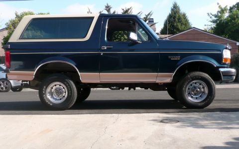 1995 Ford Bronco - Side profile of a dark blue 1995 Ford Bronco, tan lower body trim and a removable top.