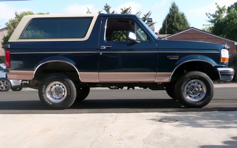 1995 Ford Bronco, dark blue with tan trim, side view. Lifted suspension and original tires visible