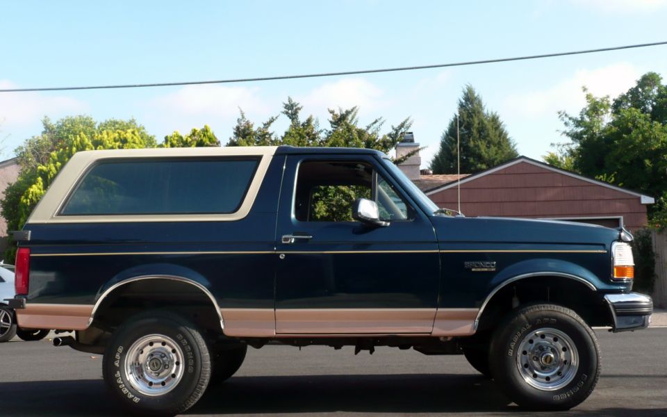 Dark blue Ford Bronco with tan trim and a removable tan top, parked outside a house