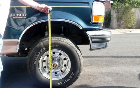1995 Ford Bronco - Measuring the ground clearance of a teal 1995 Ford Bronco, highlighting its lifted stance.