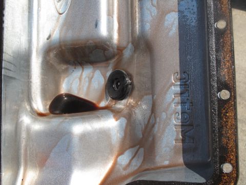 1995 Ford Bronco - Transmission pan interior with fluid pooled near the drain plug. Stamped lettering is visible on the side.