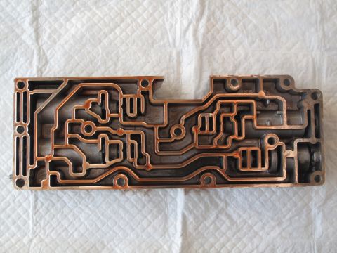 1995 Ford Bronco - This metal valve body displays intricate channels and some signs of rust, indicating it is a mechanical part.