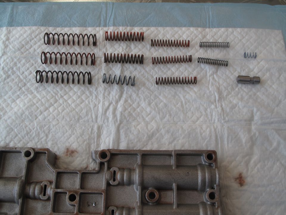 Transmission valve body and assorted springs laid out on a white textured surface