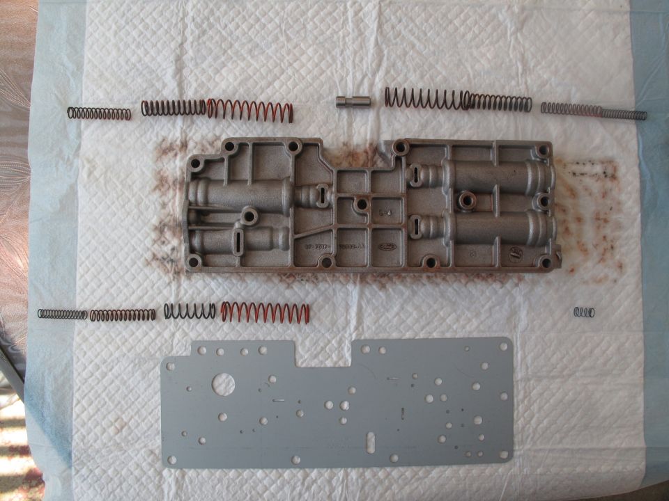 Transmission valve body disassembled with springs and a metal plate laid out on a white absorbent pad