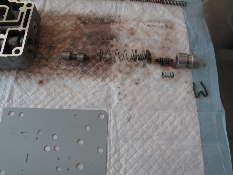 Disassembled transmission valve body with springs, pistons, and a metal plate on a white absorbent mat