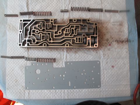 1995 Ford Bronco - Disassembled transmission valve body and springs laid out on a mat, with a metal plate below.