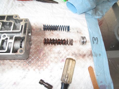 1995 Ford Bronco - Disassembled transmission valve body components, including springs and a pin, laid out with tools on a workbench.