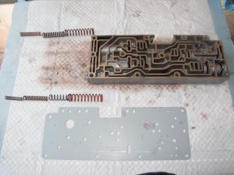 1995 Ford Bronco - Disassembled transmission valve body and springs are laid out on a cloth, with a metal plate beneath.